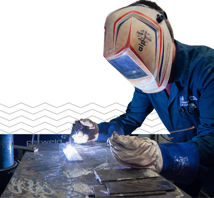 Person wearing a welding helmet and gloves while performing welding on a metal surface.
