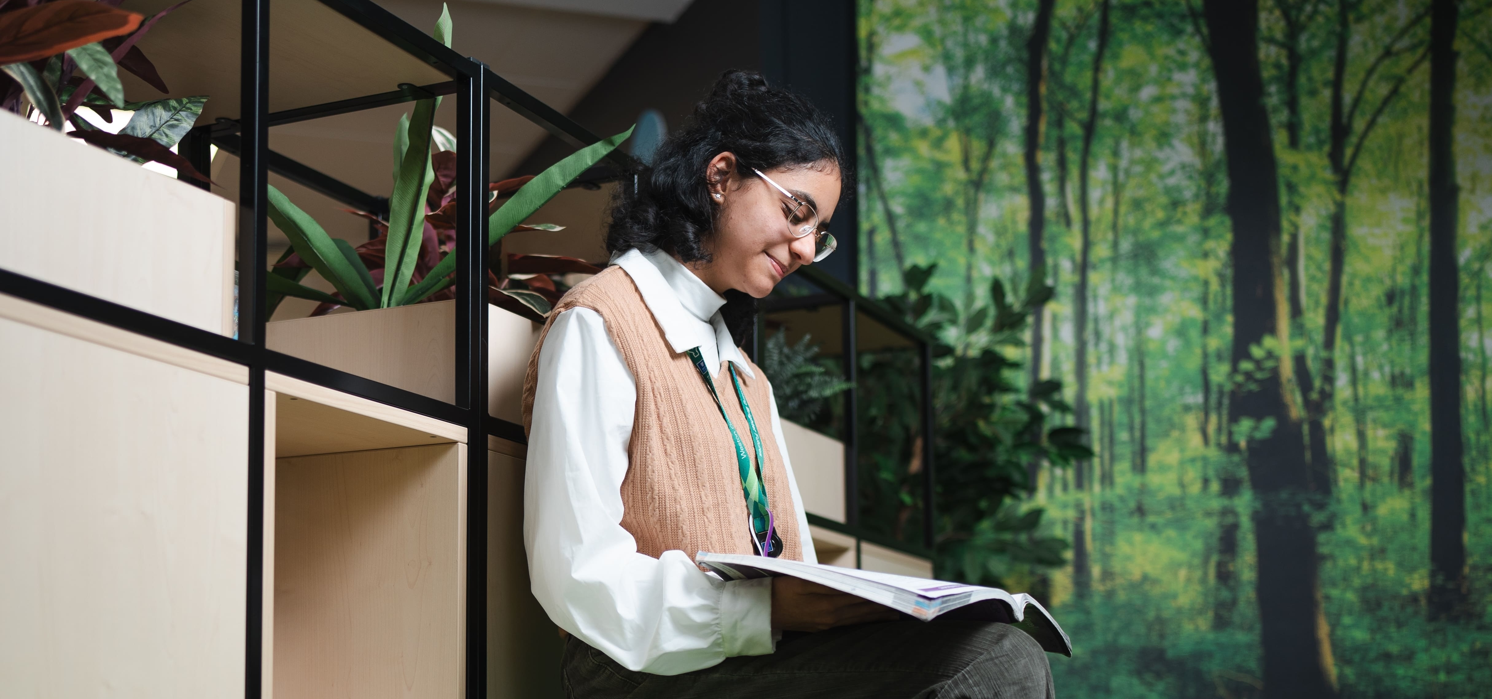 a girl sitting on a ledge in a green classroom reading a book