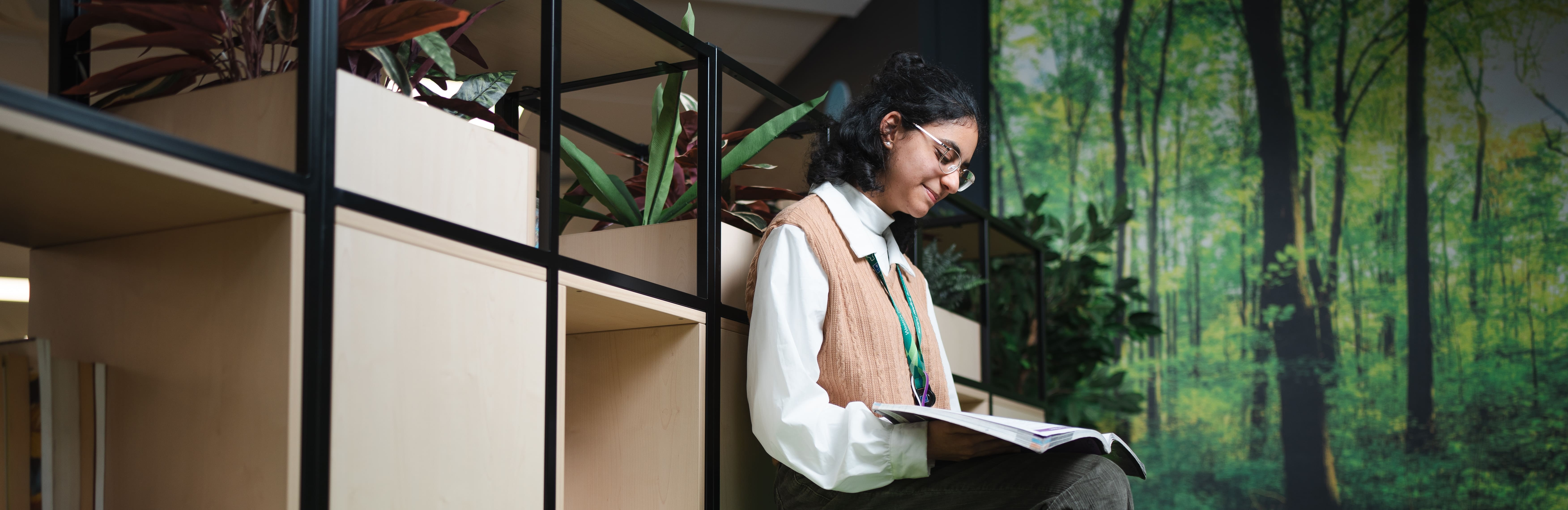 a girl sitting on a ledge in a green classroom reading a book