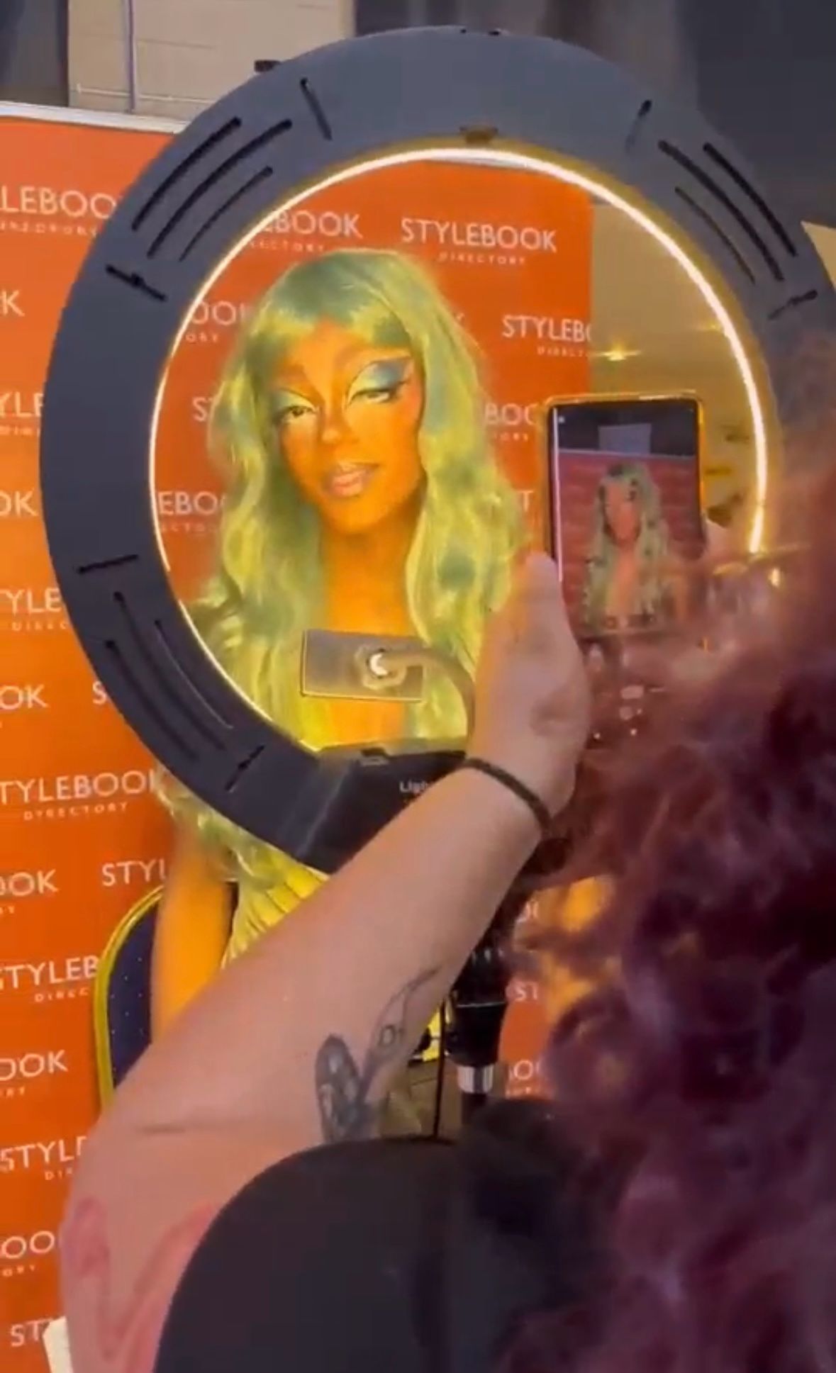 Student face painted orange with a long green wig