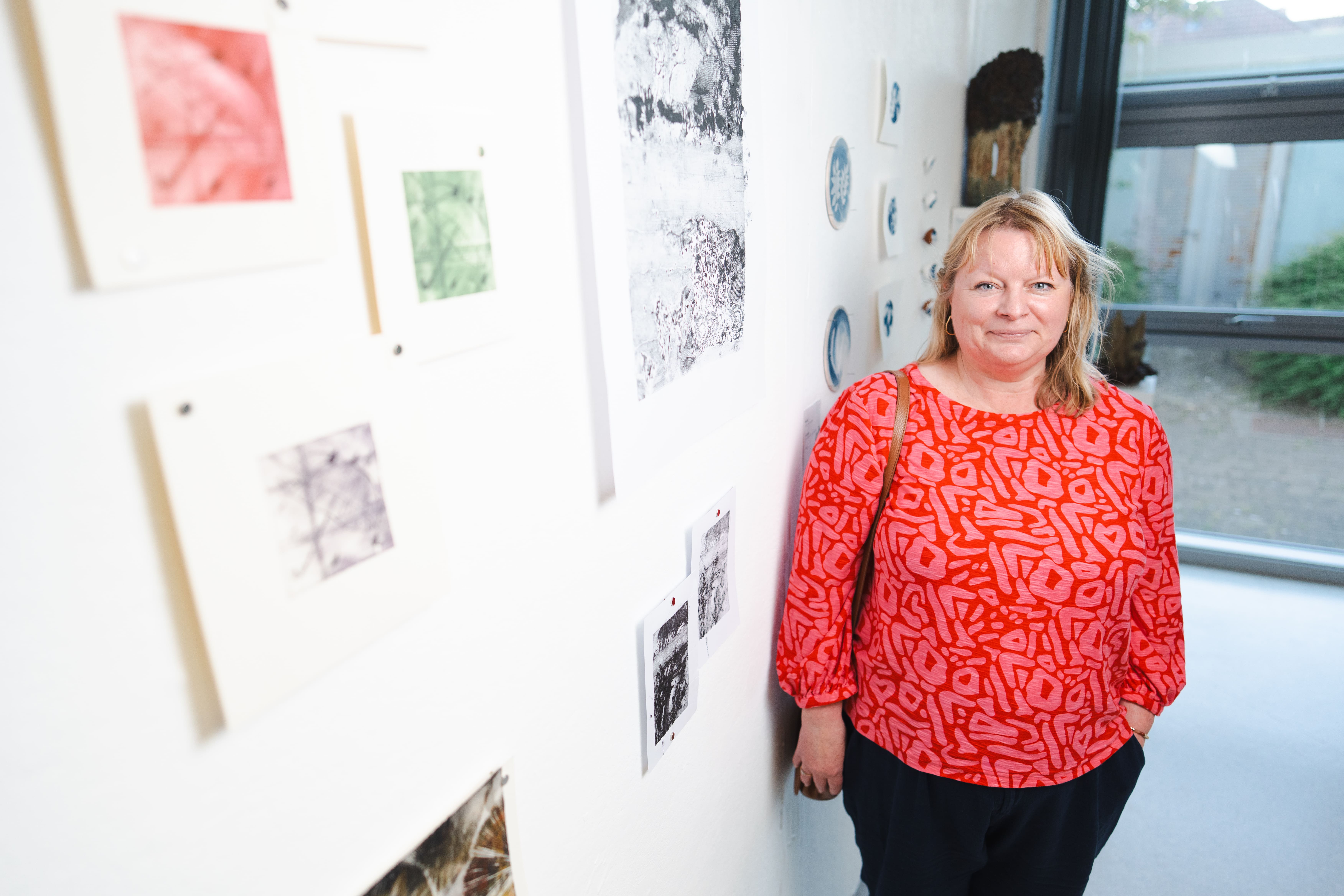 a women stands next to her abstract paintings 