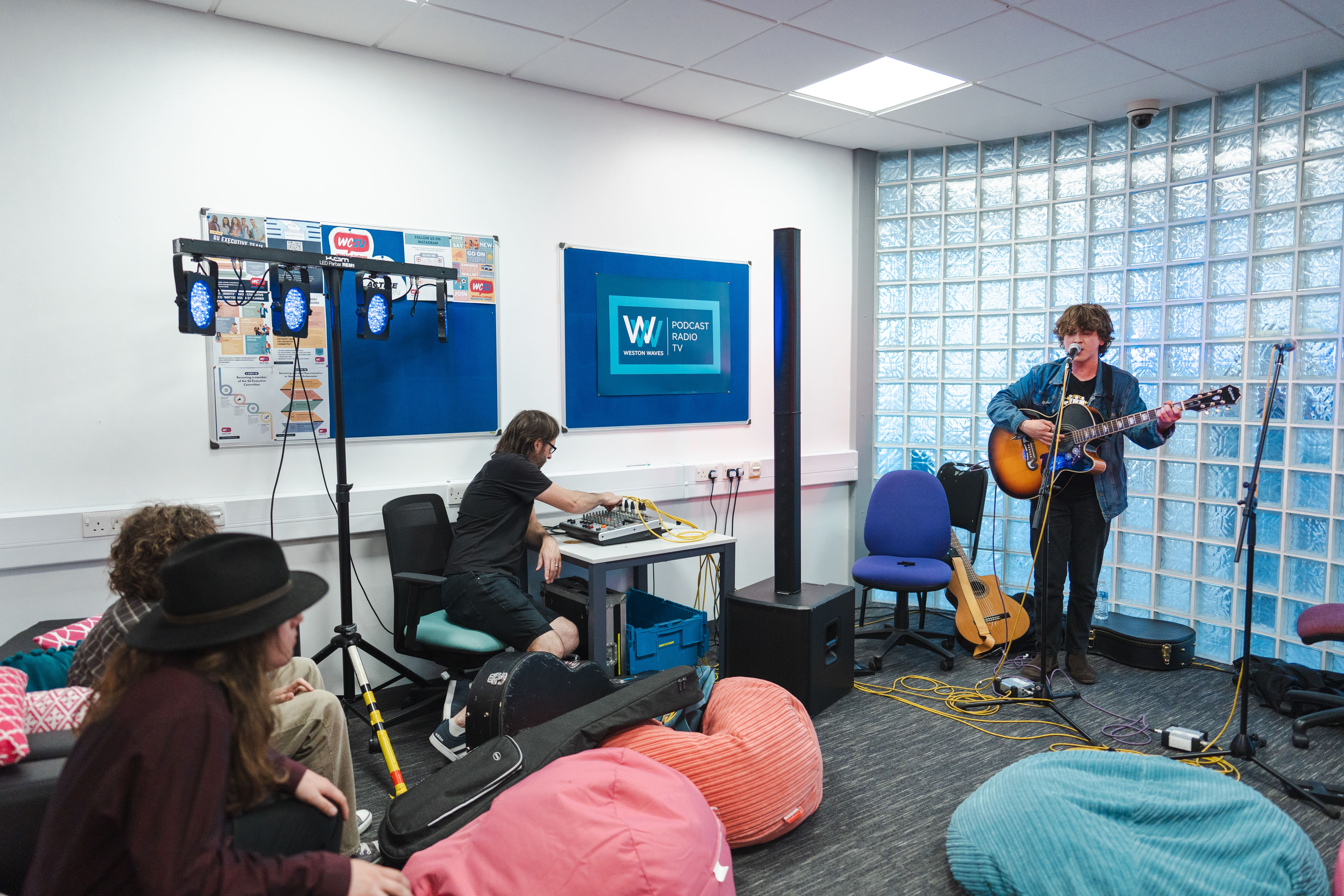a man plays the guitar and a man in a hat looks interested