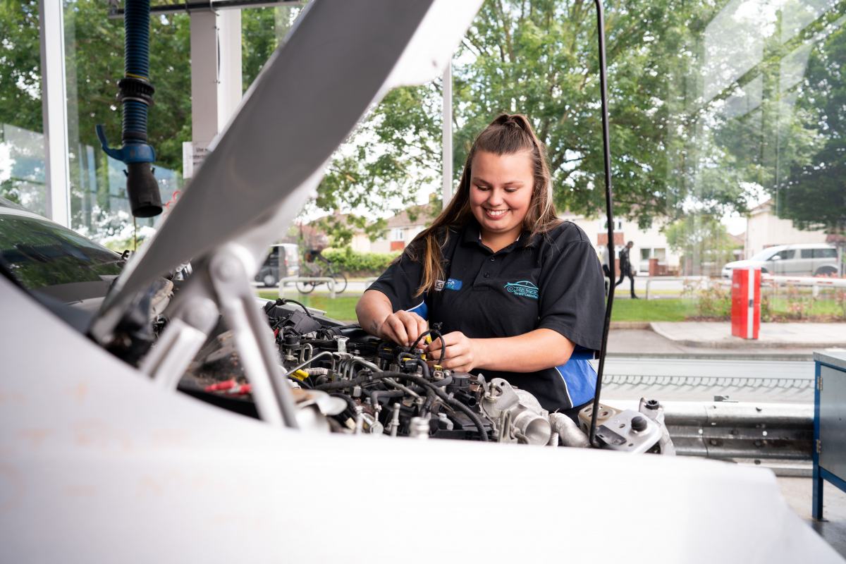 a girl works under the bonnet of a car