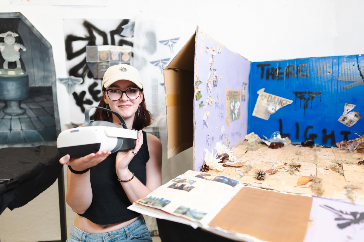 Student sat with her art project and holding a VR headset 