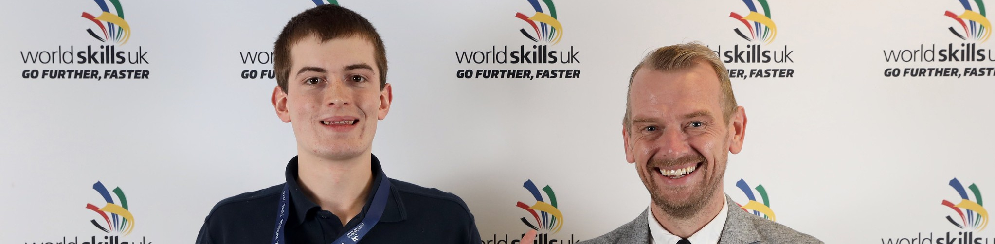 joel standing pointing at his medal with man next to him