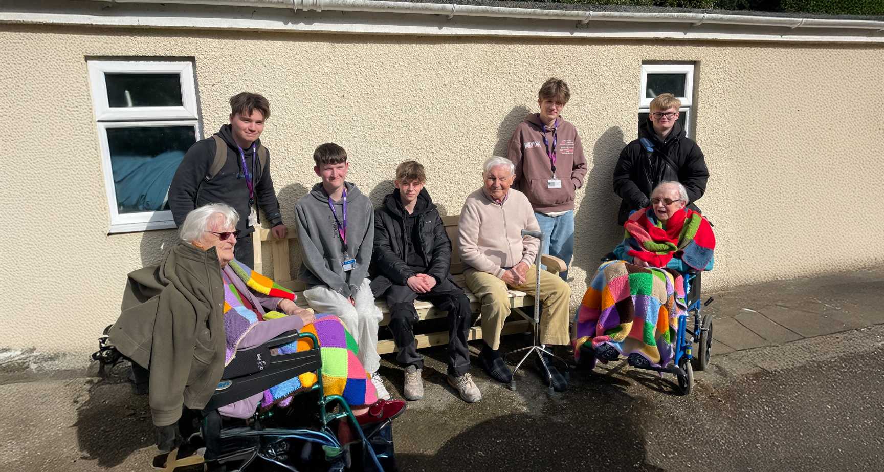 5 students and 3 residents sat on and around the bench smiling