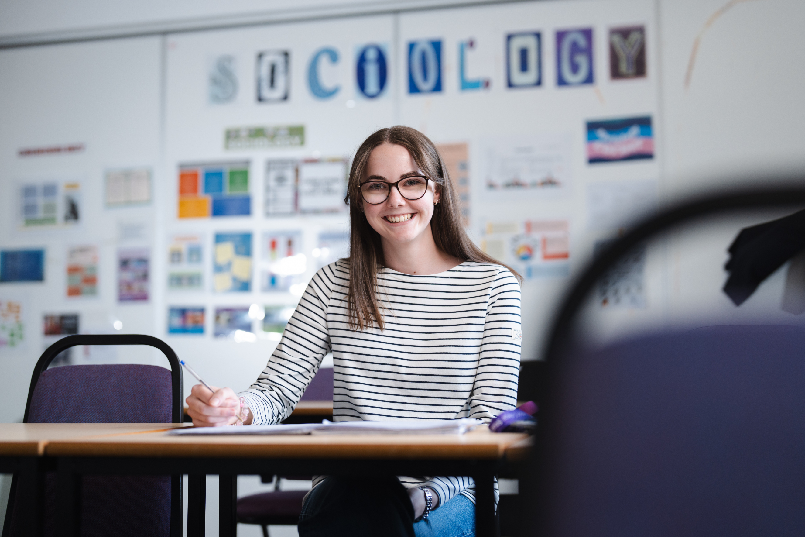 Student sat smiling whilst writing in a book
