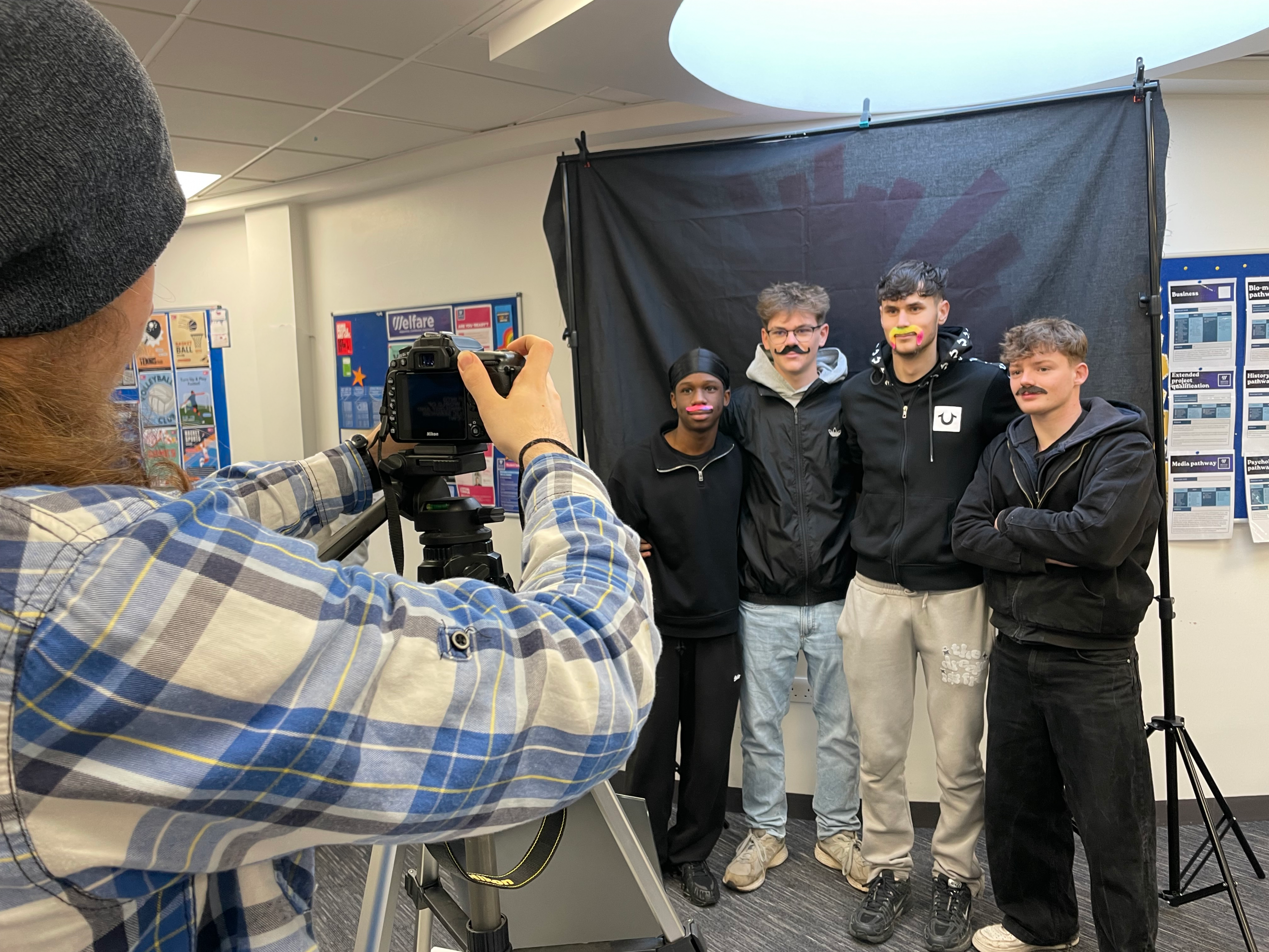 Students smiling with moustaches on in front of the camera