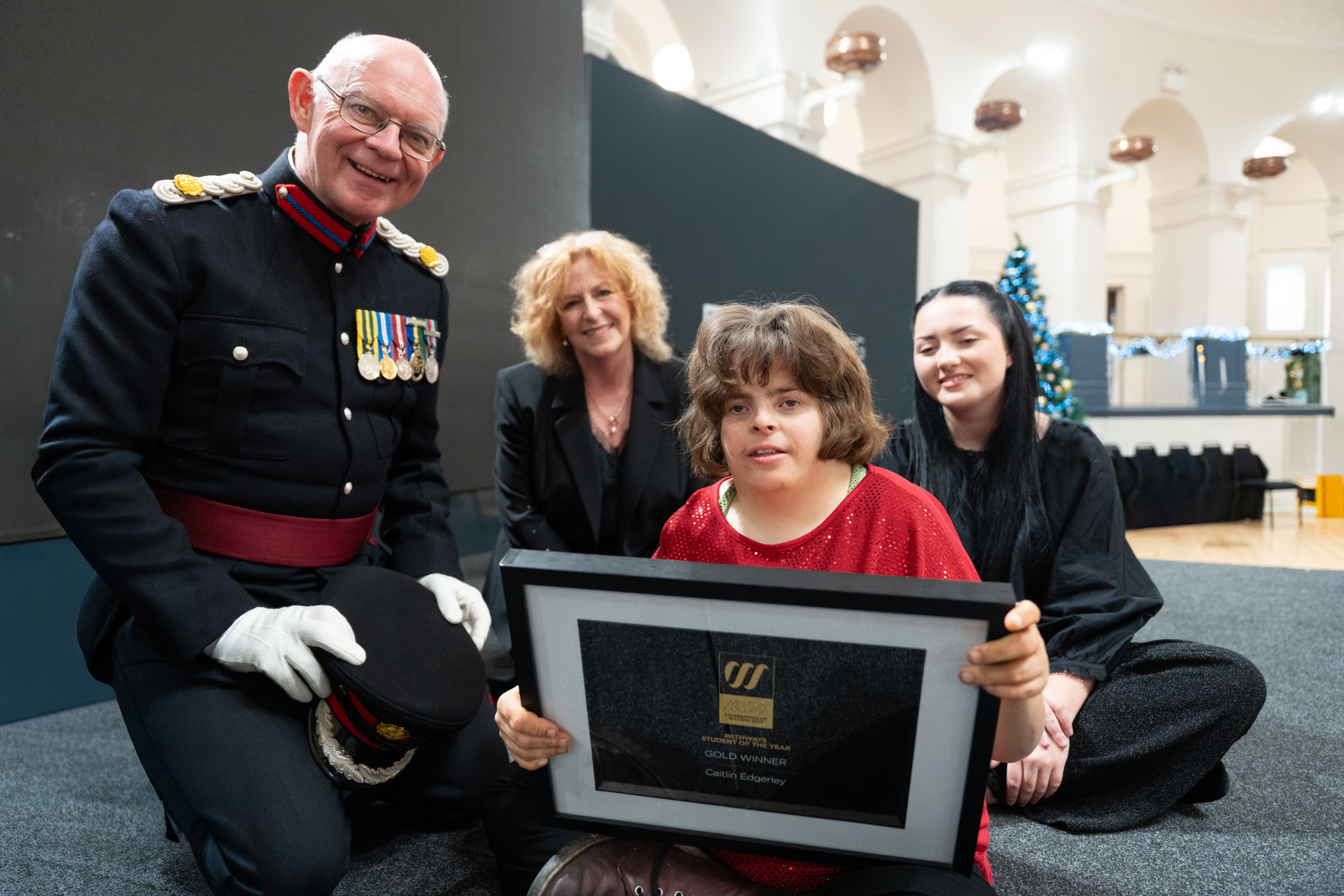 Caitlin on stage holding her award next to Brigadier Nigel Beacom