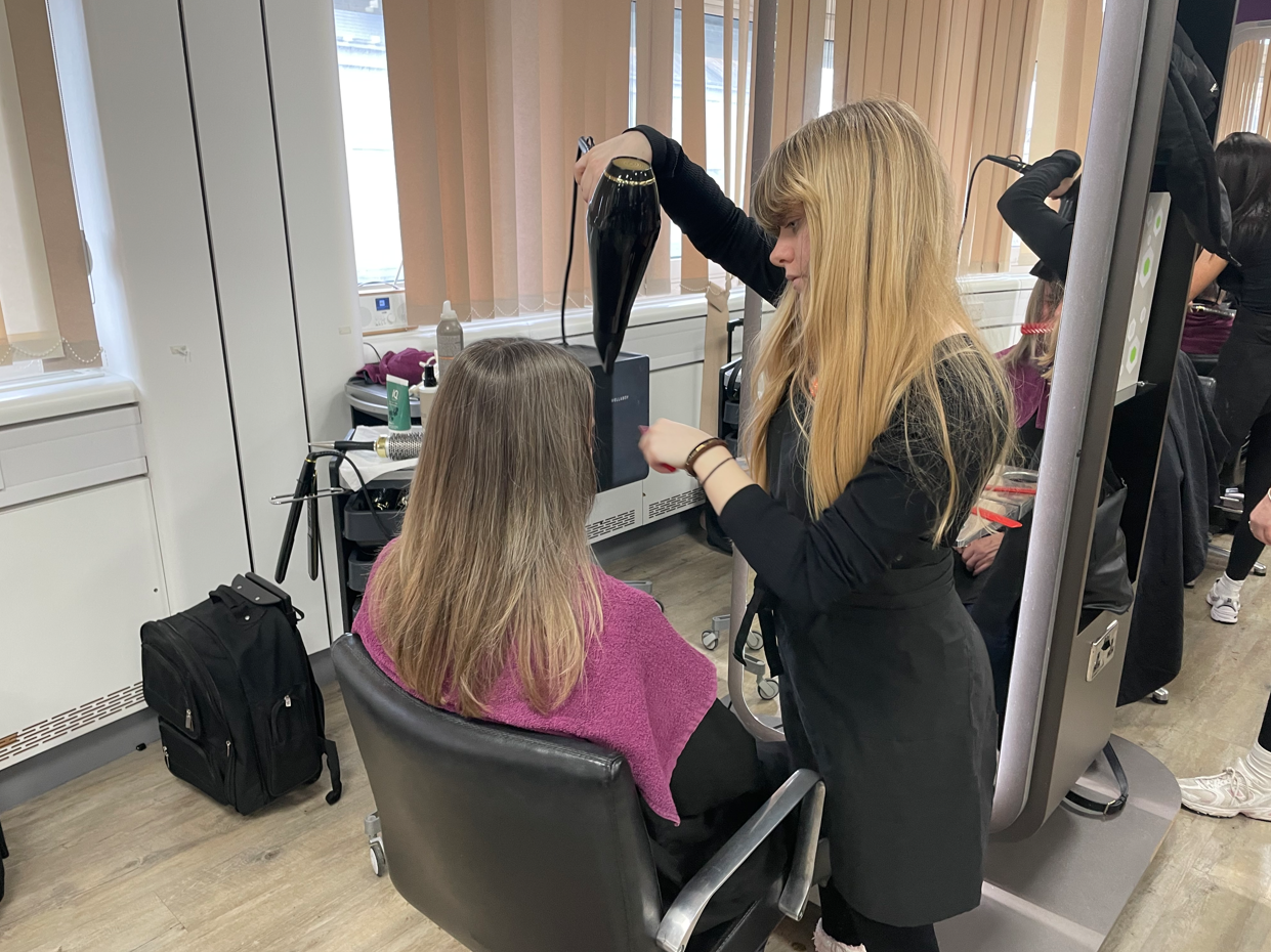 Student blow-drying a member of the public's hair