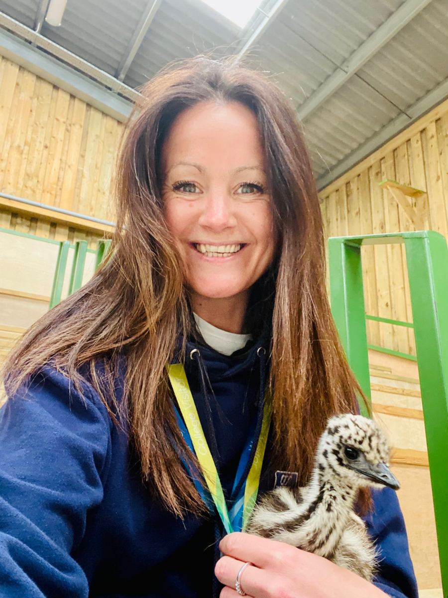 Female member of staff smiling holding baby emu