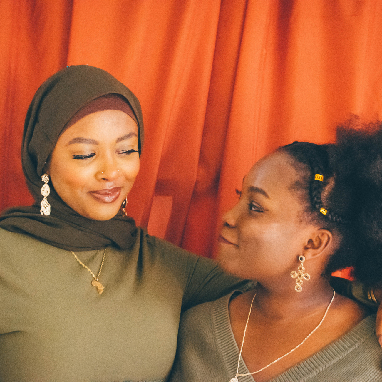 Two women looking at eachother against red curtain