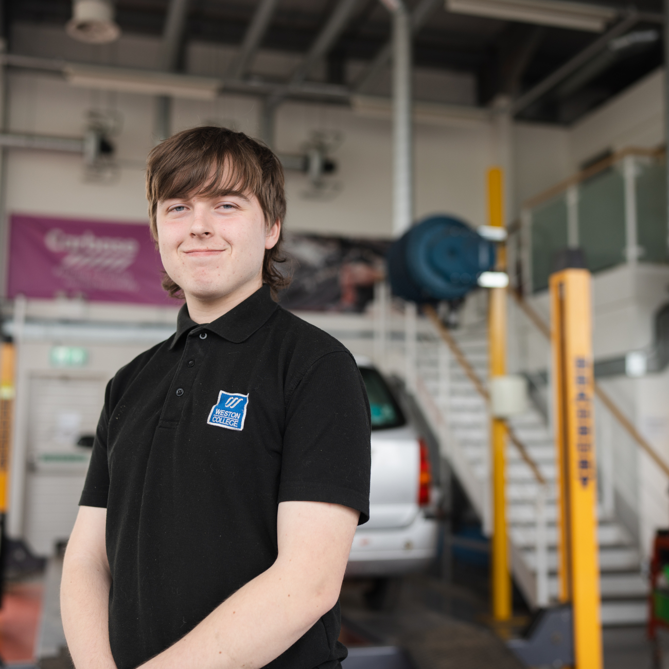 Student smiling at camera in an automotive workshop