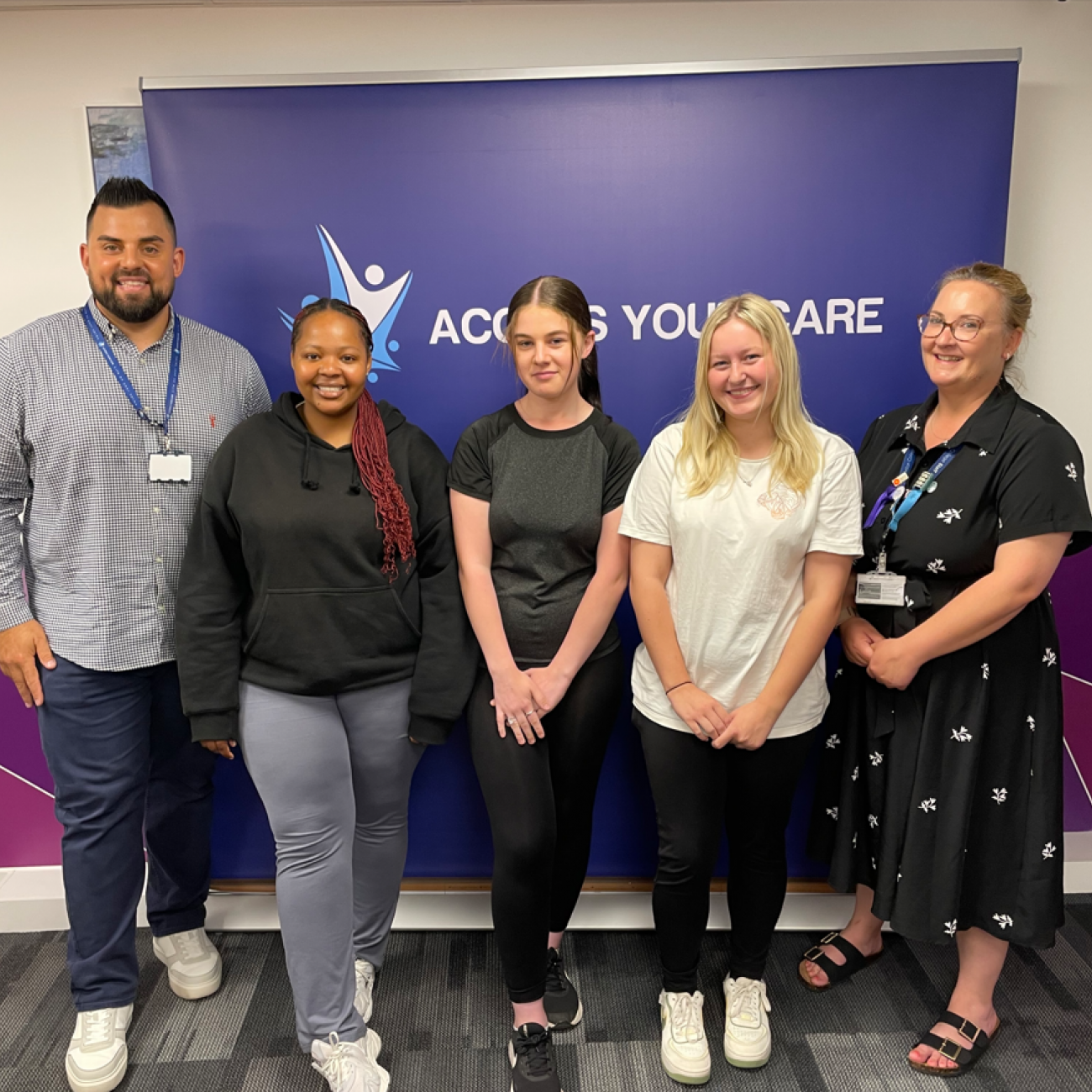 3 students, Caitlin their lecturer, and the CEO of Access Your Care in front of an Access Your Care banner