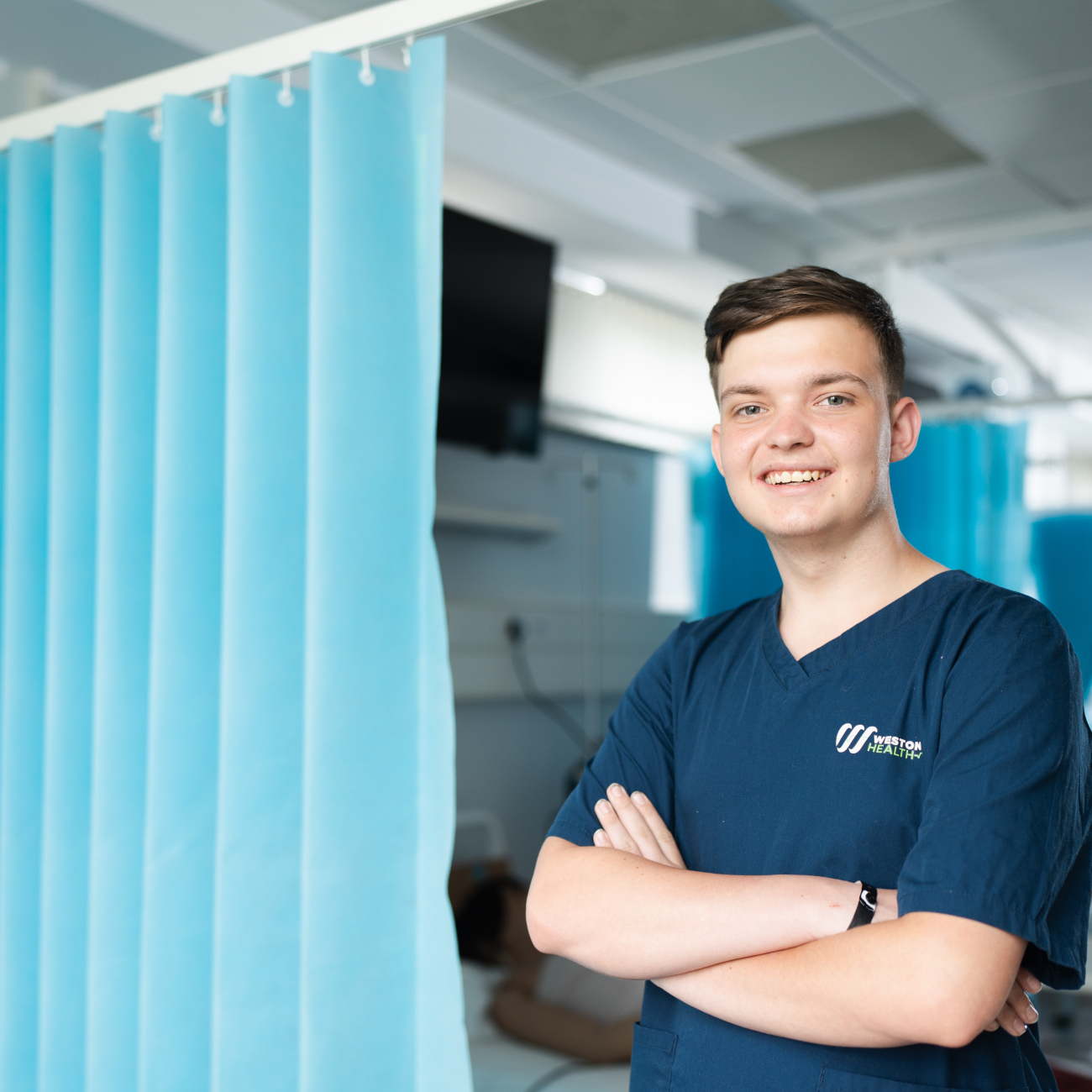 Health student wearing scrubs whilst smiling in the Simulation lab