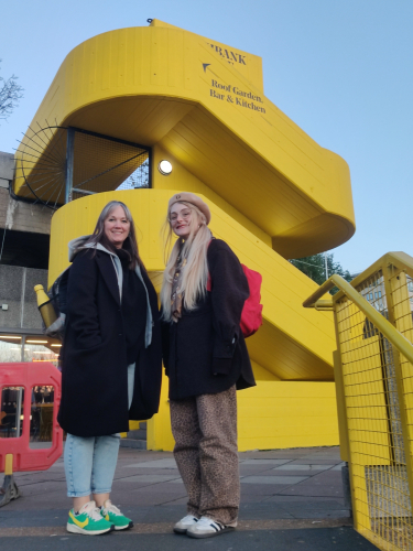 Lecturers Ronnie and Kelly smiling in front of Southbank yellow building