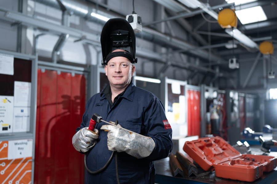 James standing wearing welding gloves and mask, holding a blow touch